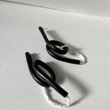 Load image into Gallery viewer, Close-up of Pearl Twist Earrings featuring twisted black leather loops paired with a strand of white pearls. The sculptural, lightweight design is bold and unusual, handcrafted from sustainable materials to create a modern statement piece."