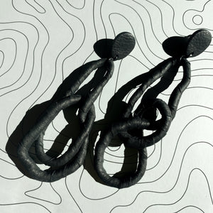 Crafted for bold style, these earrings feature a flexible wire wrapped in soft black leather, creating a unique design. With a long dangle-wrap style, they add drama to any outfit, while remaining lightweight for all-day comfort. The black leather wrapping adds texture and sophistication, offering an edgy yet elegant touch to your look.