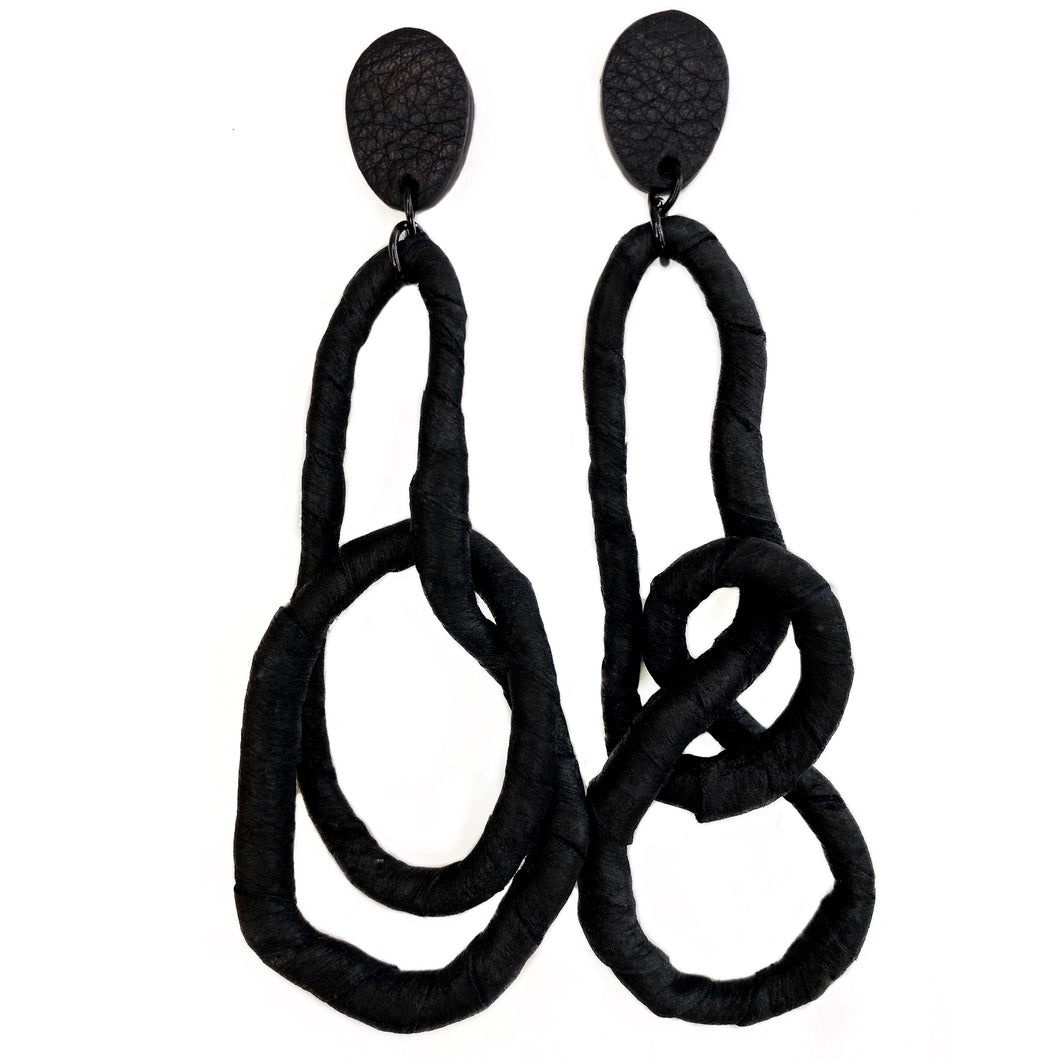 Crafted for bold style, these earrings feature a flexible wire wrapped in soft black leather, creating a unique design. With a long dangle-wrap style, they add drama to any outfit, while remaining lightweight for all-day comfort. The black leather wrapping adds texture and sophistication, offering an edgy yet elegant touch to your look.
