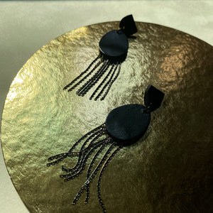 Discover our 'Affinity' Black Leather Earrings. These earrings combine sleek black leather in a stud-style semicircle and an elongated oval pendant adorned with delicate chains. The design balances modern allure and timeless charm. Perfect for formal occasions or adding a touch of noir luxury. Lightweight and elegant, these earrings embody sophistication in motion