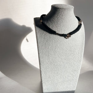 Handcrafted necklace featuring black leather discs, glossy obsidian stones, and translucent smoky quartz gemstones, designed with a bold and modern aesthetic.