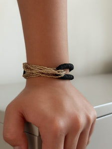 Hand wearing a gold and black bracelet on a neutral background