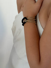 Load image into Gallery viewer, Handcrafted bracelet with golden glass beads interlocked with black leather strand on a model.
