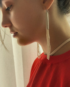Close-up of a person wearing long earrings with a neutral background