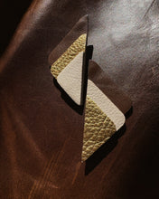 Load image into Gallery viewer, A pair of geometric leather earrings with a textured gold and cream pebbled finish, displayed on a dark brown leather surface.