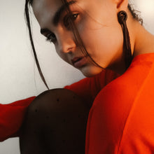 Load image into Gallery viewer, Close-up of a person wearing brown long beaded leather  earrings and a red garment with a neutral background
