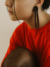 Load image into Gallery viewer, Close-up of a person wearing brown long beaded leather  earrings and a red garment with a neutral background