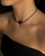 Load image into Gallery viewer, Person wearing a black necklace with a small pendant on a dark background