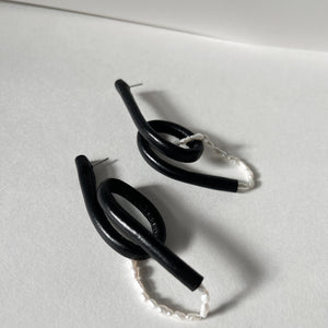 Close-up of Pearl Twist Earrings featuring twisted black leather loops paired with a strand of white pearls. The sculptural, lightweight design is bold and unusual, handcrafted from sustainable materials to create a modern statement piece."