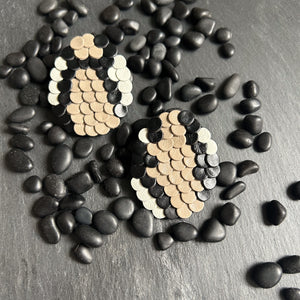 Close-up of snake-inspired earrings made from black, beige, and white leather. The layered design resembles scales, featuring a bold mosaic pattern with a textured, modern look. Handcrafted from upcycled leather, they are lightweight and sustainable.