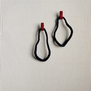 A pair of reshapable earrings handcrafted from black leather with a textured finish, forming irregular looped shapes, accented by bold red leather connectors. Lightweight and versatile for unique styling.