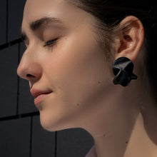 Load image into Gallery viewer, Close-up of Rivelis Earrings, featuring a unique, multi-dimensional design crafted from black, supple leather. The earrings have a nature-inspired, fluid shape that is both lightweight and elegant.