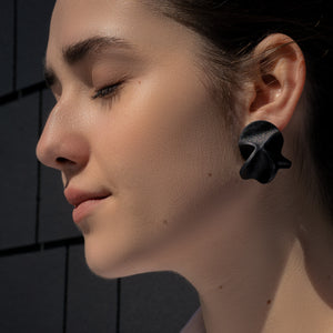 Close-up of Rivelis Earrings, featuring a unique, multi-dimensional design crafted from black, supple leather. The earrings have a nature-inspired, fluid shape that is both lightweight and elegant.