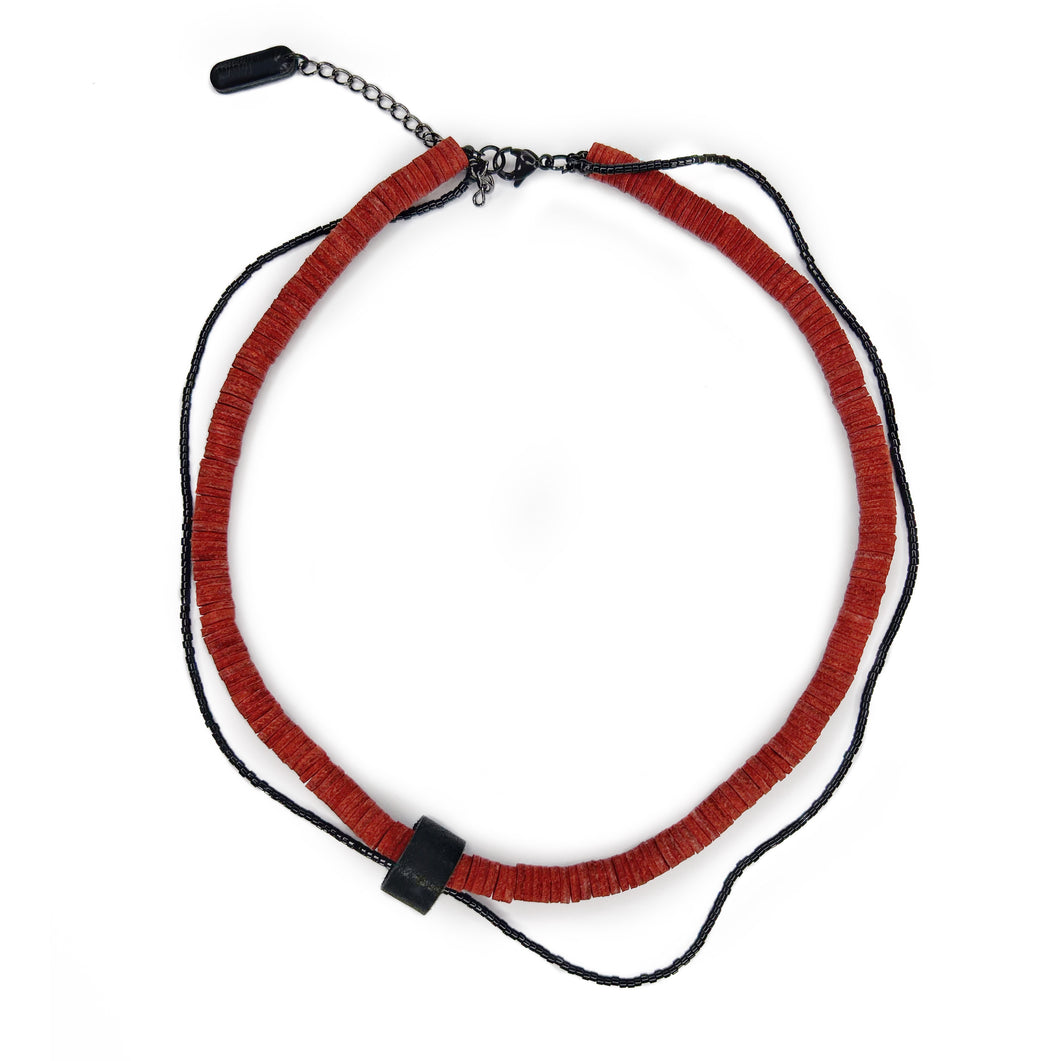 Close-up of red leather disk choker with hand-stitched black leather tube and thin black glass bead string worn on neck