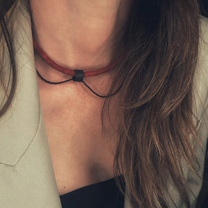 Close-up of red leather disk choker with hand-stitched black leather tube and thin black glass bead string worn on neck