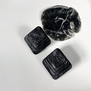 Square black leather earrings with rounded corners, featuring layered leather design for a dimensional and sculptural look.