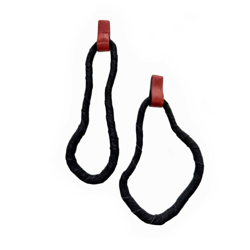 A pair of reshapable earrings handcrafted from black leather with a textured finish, forming irregular looped shapes, accented by bold red leather connectors. Lightweight and versatile for unique styling.