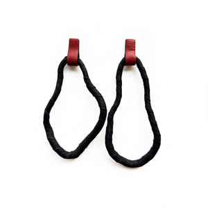 A pair of reshapable earrings handcrafted from black leather with a textured finish, forming irregular looped shapes, accented by bold red leather connectors. Lightweight and versatile for unique styling.