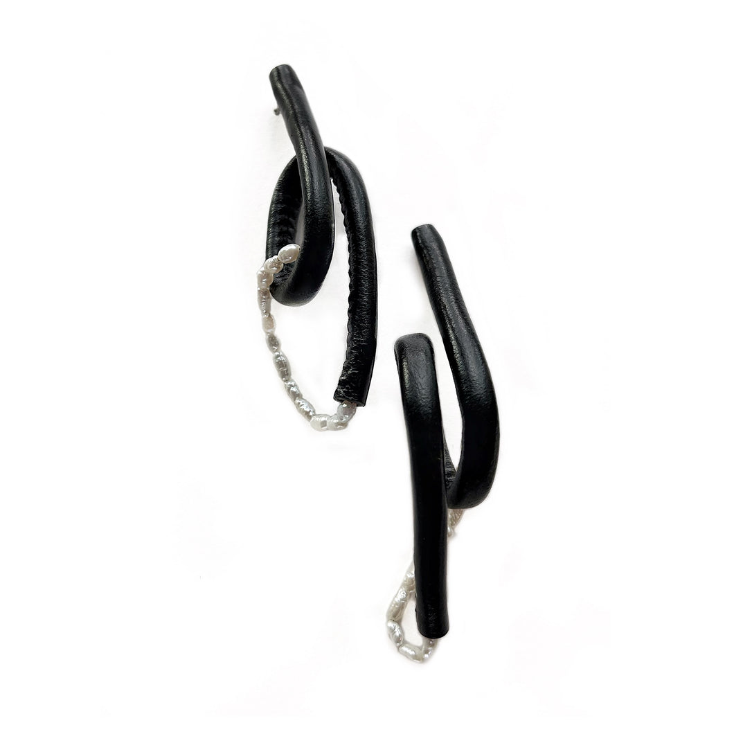 Close-up of Pearl Twist Earrings featuring twisted black leather loops paired with a strand of white pearls. The sculptural, lightweight design is bold and unusual, handcrafted from sustainable materials to create a modern statement piece.