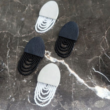 Load image into Gallery viewer, Off-white and black leather earrings with cascading white translucent and shiny black bead layers, featuring a textured finish and lightweight, modern design.
