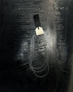 Close-up of  a dangling leather glass bead earring on a dark textured background