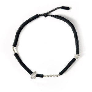 Handcrafted necklace featuring black leather discs, freshwater pearls, and clear quartz gemstones, designed with a modern, tactile aesthetic.