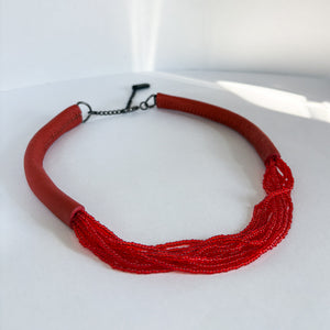 A choker that pairs hand-stitched leather with cascading strands of glass beads. The tubular leather form gives it presence, while the beads add fluid movement in a striking red. Lightweight and adjustable, made for moments that stand out.
