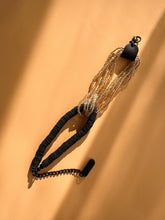 Load image into Gallery viewer, Handcrafted bracelet with golden glass beads interlocked with black leather disks and adjustable chain on a beige background