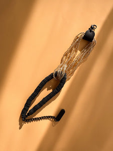Handcrafted bracelet with golden glass beads interlocked with black leather disks and adjustable chain on a beige background