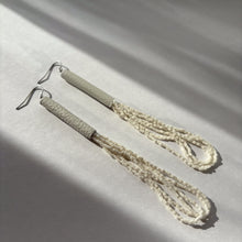 Load image into Gallery viewer, A pair of handcrafted earrings with ivory leather cylindrical tops, cascading strands of white glass seed beads, and hypoallergenic stainless steel hooks.