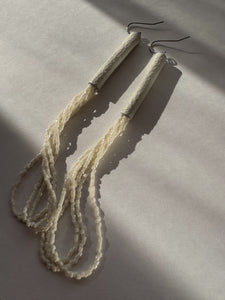 Pair of beige thread earrings on a light gray background