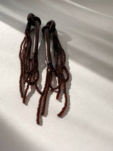 Load image into Gallery viewer, A pair of handcrafted earrings with knotted espresso leather tops, cascading strands of brown glass beads, and stainless steel studs, photographed on a white background.