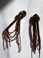 Load image into Gallery viewer, A pair of handcrafted earrings with knotted espresso leather tops, cascading strands of brown glass beads, and stainless steel studs, photographed on a white background.