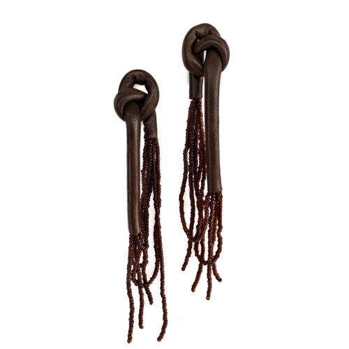 A pair of handcrafted earrings with knotted espresso leather tops, cascading strands of brown glass beads, and stainless steel studs, on a white background.