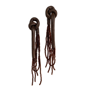 A pair of handcrafted earrings with knotted espresso leather tops, cascading strands of brown glass beads, and stainless steel studs, on a white background.