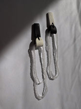 Load image into Gallery viewer, Mismatched earrings combining black and white leather tops with cascading strands of transparent glass beads.