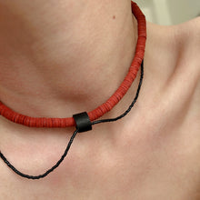 Load image into Gallery viewer, Close-up of red leather disk choker with hand-stitched black leather tube and thin black glass bead string worn on neck