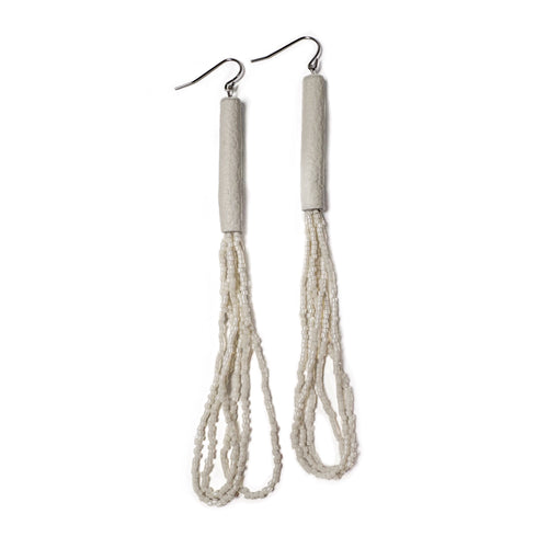A pair of handcrafted earrings with ivory leather cylindrical tops, cascading strands of white glass seed beads, and hypoallergenic stainless steel hooks.