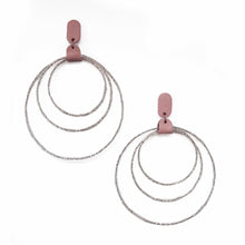 Load image into Gallery viewer, A pair of dangling earrings with three textured silver-tone concentric rings attached to a dusty rose pink rectangular stud, shown on a plain white background.