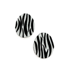 Load image into Gallery viewer, Close-up of earrings featuring a white leather base with bold, hand-cut black zebra stripes. The modern design showcases sharp contrast and wild energy, blending edgy patterns with effortless style. Lightweight and handcrafted from sustainable materials, these earrings are part of a nature-inspired collection.