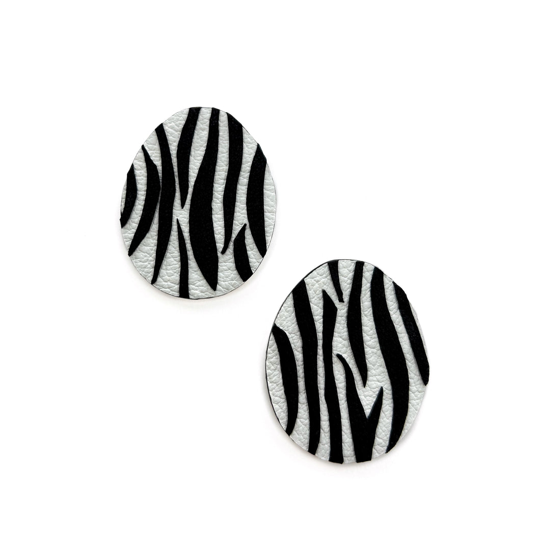 Close-up of earrings featuring a white leather base with bold, hand-cut black zebra stripes. The modern design showcases sharp contrast and wild energy, blending edgy patterns with effortless style. Lightweight and handcrafted from sustainable materials, these earrings are part of a nature-inspired collection.