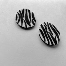 Load image into Gallery viewer, Close-up of earrings featuring a white leather base with bold, hand-cut black zebra stripes. The modern design showcases sharp contrast and wild energy, blending edgy patterns with effortless style. Lightweight and handcrafted from sustainable materials, these earrings are part of a nature-inspired collection.