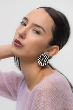 Load image into Gallery viewer, Close-up of earrings featuring a white leather base with bold, hand-cut black zebra stripes. The modern design showcases sharp contrast and wild energy, blending edgy patterns with effortless style. Lightweight and handcrafted from sustainable materials, these earrings are part of a nature-inspired collection.