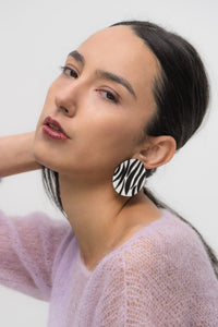 Close-up of earrings featuring a white leather base with bold, hand-cut black zebra stripes. The modern design showcases sharp contrast and wild energy, blending edgy patterns with effortless style. Lightweight and handcrafted from sustainable materials, these earrings are part of a nature-inspired collection.