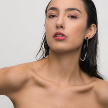 Load image into Gallery viewer, Close-up of a model wearing Pearl Twist Earrings. The earrings feature twisted black leather loops with a strand of white pearls, creating a bold and sculptural look. The lightweight design adds a unique, modern touch to the model’s outfit.