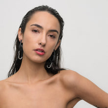 Load image into Gallery viewer, Close-up of a model wearing Pearl Twist Earrings. The earrings feature twisted black leather loops with a strand of white pearls, creating a bold and sculptural look. The lightweight design adds a unique, modern touch to the model’s outfit.