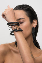 Load image into Gallery viewer, A bold, handcrafted bracelet made with individually hand-punched black leather discs, a sleek hand-stitched leather tube, and delicate black glass beads. The layered, wraparound design creates a modern and textured statement piece.